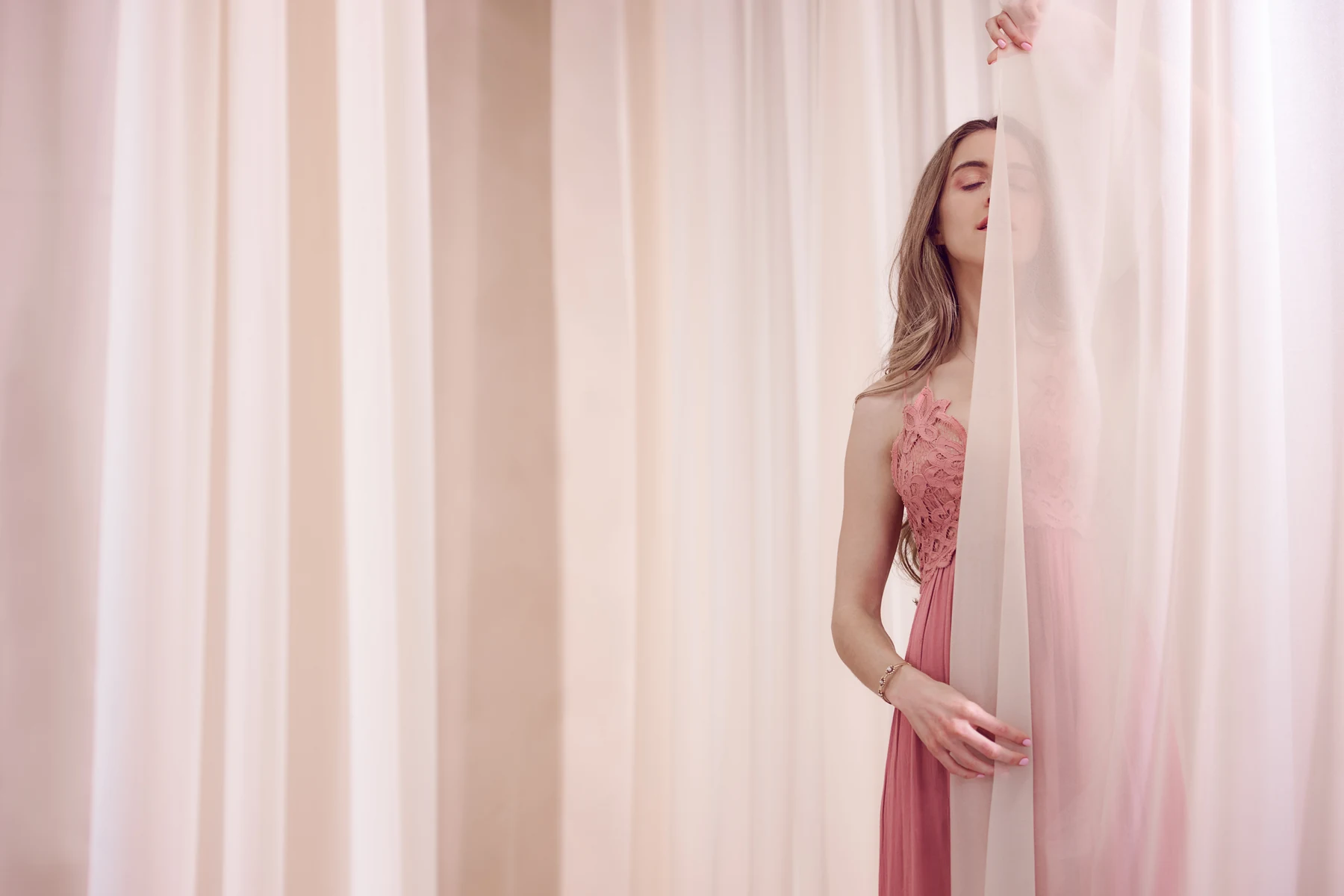 Marissa in a pink dress, eyes closed behind soft sheer curtains.